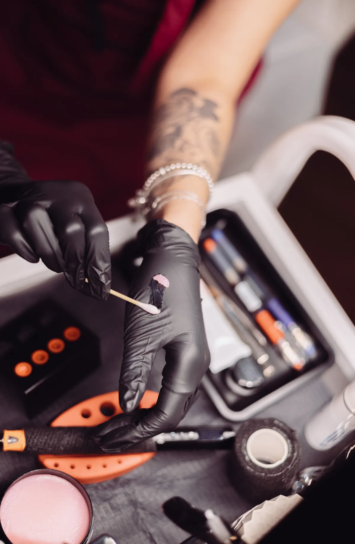 Black nitrile gloves and a tray of sterile tattoo tools and ink laid out on the bench
